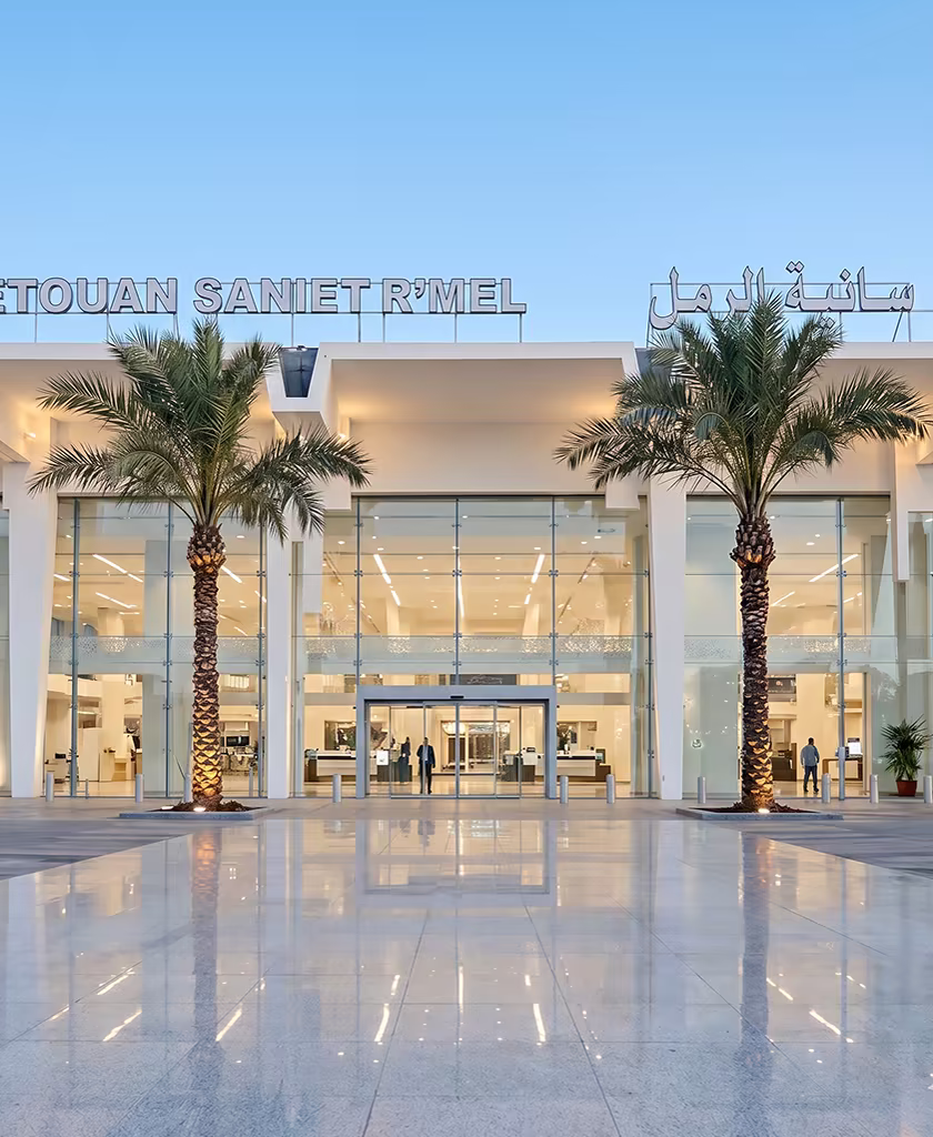 Entrée illuminée du terminal de l'aéroport de Tétouan-Saniat R'mel (TTU) au crépuscule, encadrée de palmiers